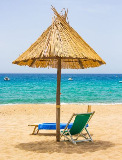 a beach chair facing the sea under a beach umbrella