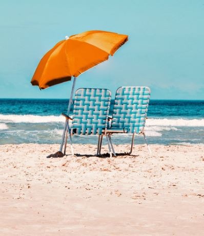 two beach chairs shaded with an orange umbrella