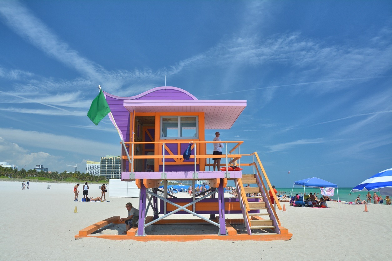 a green flag flying at a purple lifeguard tower in South Beach, Miami Beach flocked with people