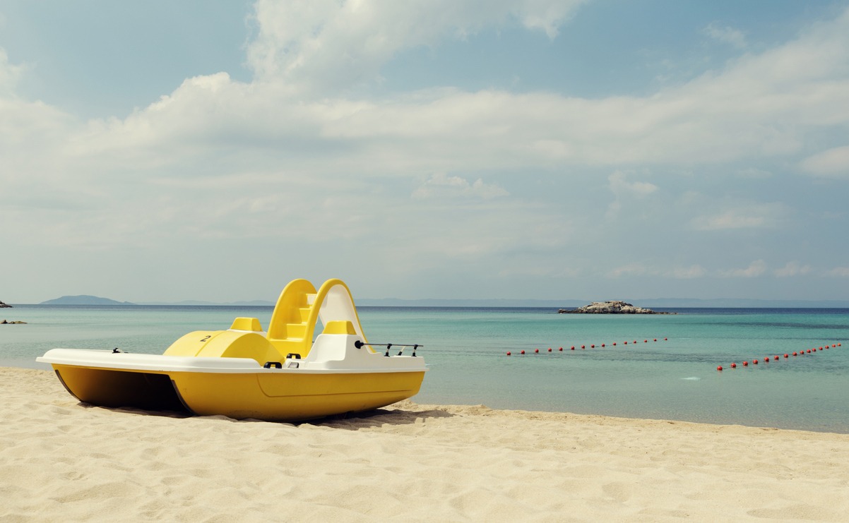 a yellow pedal boat on a turquoise beach in Greece and lines with red buoys