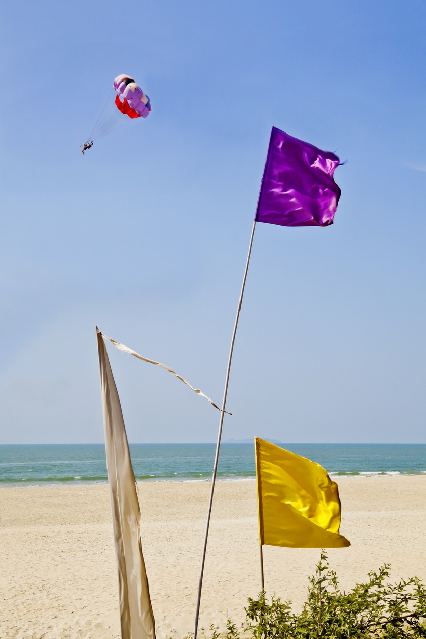 yellow and purple flags blowing in the breeze outside a shack restaurant in Goa India on Uttorda Beach with a para glider passing by in the distance