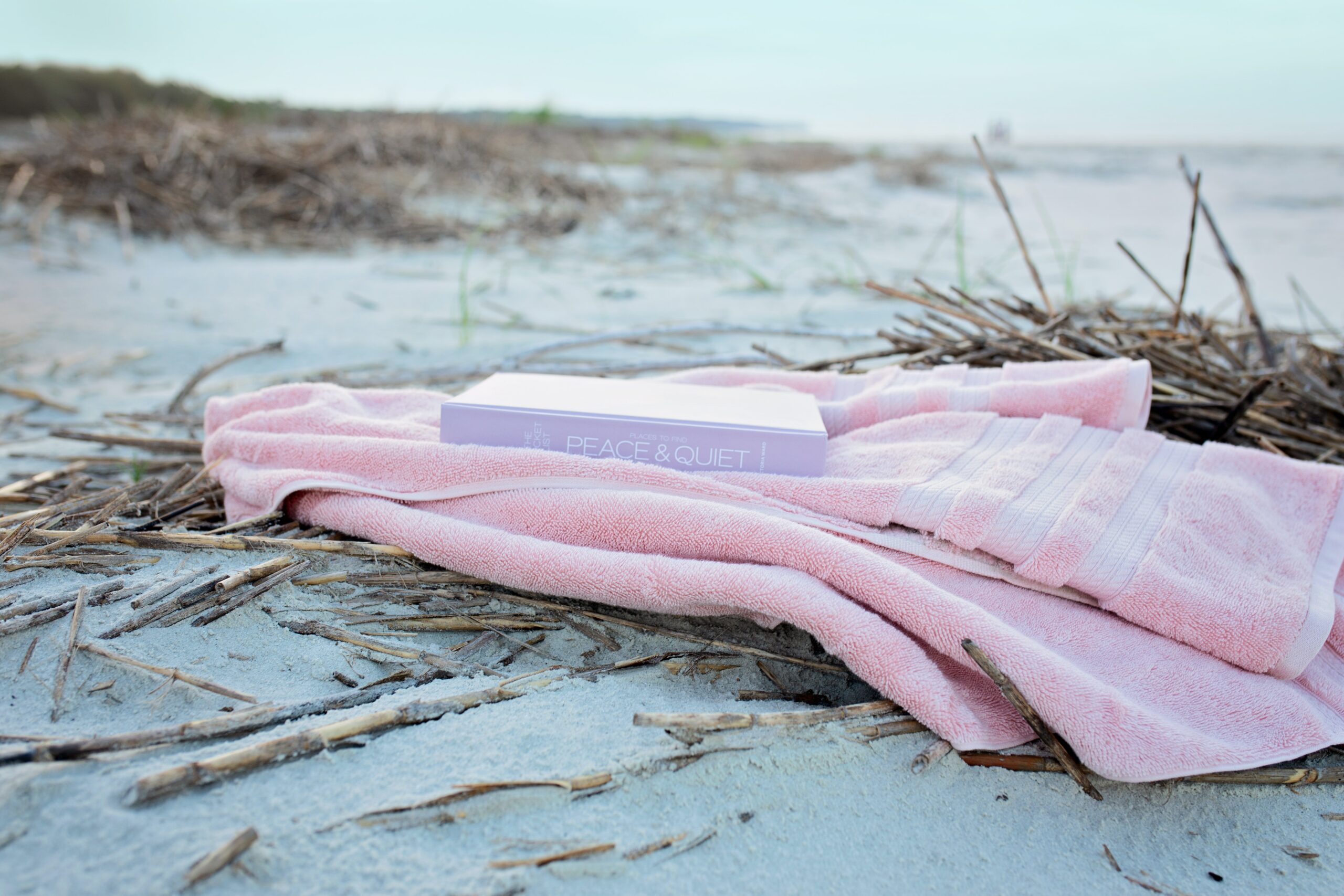 book-on-pink-textile-on-sand-during-day